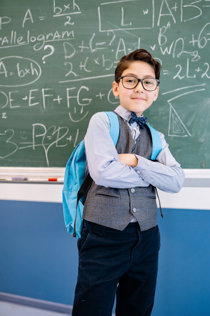 Young boy with glasses standing confidently in front of a math-filled chalkboard, embodying academic spirit.